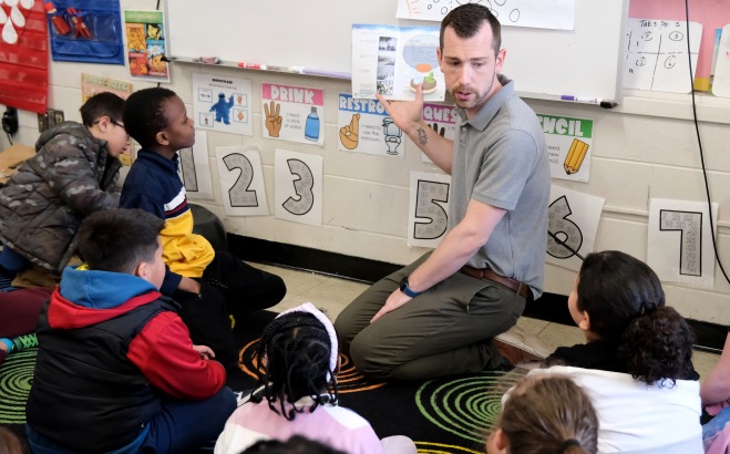 Dustin Halterman in classroom reading to a group of students