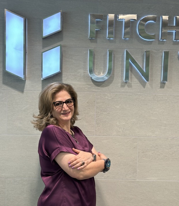 Mojdeh Bayat, Dean of Education in front of shield on the wall